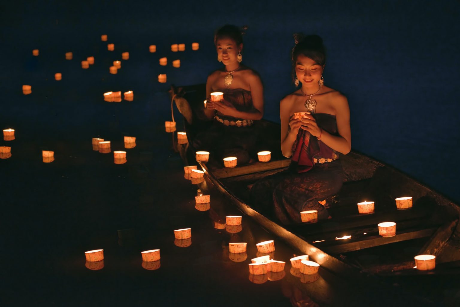 Girls in Thai traditional dress praying with lanterns for respect to the water spirit